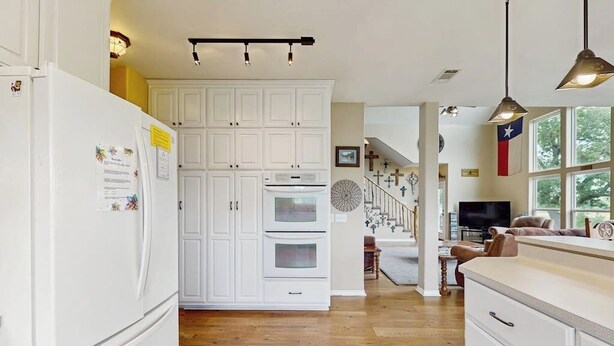 A kitchen with white cabinetry, a refrigerator, an oven, and a dining area with a TV.