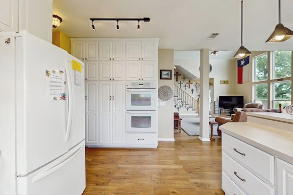 A kitchen with white cabinetry, a refrigerator, an oven, and a dining area with a TV.