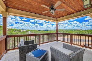 Un espacio al aire libre techado con mobiliario de mimbre, un ventilador de techo y vistas a un paisaje verde.