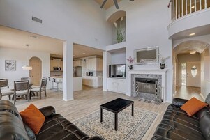 Amplia sala de estar con chimenea, sofás de cuero, una mesa de comedor y una cocina al fondo.