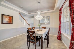 Un comedor con candelabro, sillas de madera, una mesa y una escalera.