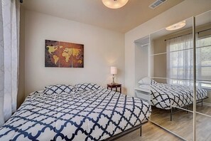 A bedroom with a bed, a bedside table with a lamp, a world map artwork, and a large mirror. - Spacious, Dog-friendly Home With Two Decks, Views, Grill, W/D & Community Pool (Leander)