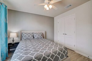 Un dormitorio con cama, mesita de noche, ventilador de techo y una puerta.