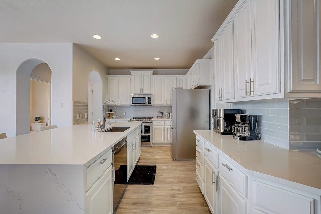 A modern kitchen with white cabinetry, a stainless steel refrigerator, a microwave, and a coffee maker.