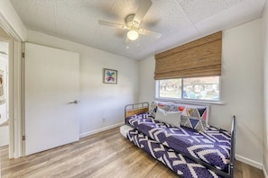 Ein Schlafzimmer mit einem Bett, einem Deckenventilator, einem Fenster mit Jalousien und einer Tür.