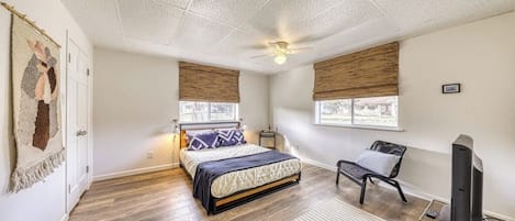 Quarto com cama, cadeira, escrivaninha, ventilador de teto e janelas com persianas.