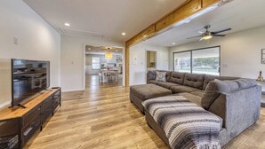 Un salon moderne avec un canapé d’angle, un téléviseur à écran plat et une poutre en bois au plafond.