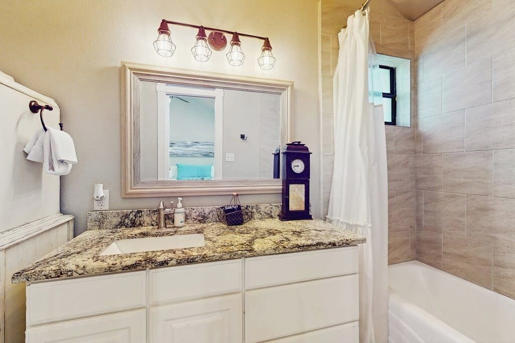 Une salle de bain avec un comptoir en granit, un grand miroir, une horloge et un rideau de douche.