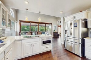 Una cocina moderna con armarios blancos, una isla grande, electrodomésticos de acero inoxidable e iluminación colgante.