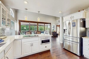 Una cocina moderna con armarios blancos, una isla grande, electrodomésticos de acero inoxidable e iluminación colgante.