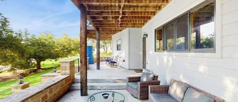 Une terrasse extérieure couverte, aménagée avec des meubles en osier, une table en verre et offrant une vue sur le paysage environnant.