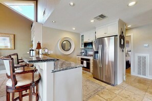 A kitchen with a central island, bar stools, a refrigerator, and a microwave. - Refined Panoramic Paradise on Lake Travis With Boat Launch and Tesla Charger (Spicewood)