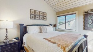 Une chambre à coucher avec un lit, une table de chevet, une lampe et une fenêtre donnant sur un immeuble.