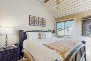 Un dormitorio con cama, mesita de noche, lámpara y ventana con vista a un edificio.