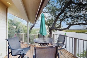 A covered outdoor deck with a table and chairs, overlooking a body of water and trees. - Refined Panoramic Paradise on Lake Travis With Boat Launch and Tesla Charger (Spicewood)