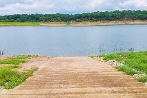 A concrete pathway leading to a body of water with a forested area in the background. - Refined Panoramic Paradise on Lake Travis With Boat Launch and Tesla Charger (Spicewood)