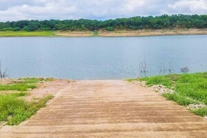 Un sendero de concreto que lleva a una masa de agua, con un área boscosa al fondo.