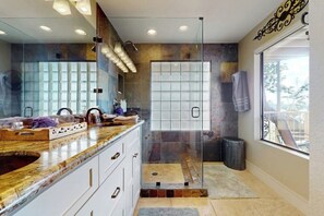 A modern bathroom with a glass shower enclosure, a marble countertop, and a large mirror. - Refined Panoramic Paradise on Lake Travis With Boat Launch and Tesla Charger (Spicewood)