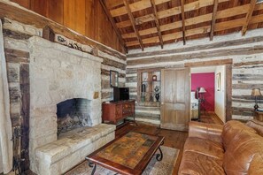 A rustic log cabin interior with a stone fireplace, leather sofa, and wooden beams. - Lovely Dog-friendly Suite With Tasting Rooms Along Hwy 290 Wine Trail (Fredericksburg)