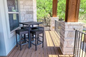 A covered outdoor area with a stone wall, a wooden deck, and a black metal table with two chairs. - Bright & Spacious Family Home With Firepit, Lake Views, Furnished Deck, Free Wifi (Leander)