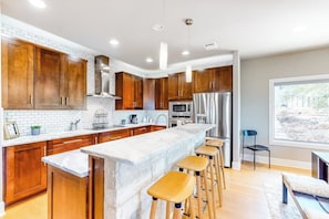 Una cocina moderna con gabinetes de madera, una isla de mármol y taburetes de bar.