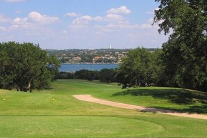A golf course with a water body in the background, surrounded by trees and buildings. - Bright & Spacious Family Home With Firepit, Lake Views, Furnished Deck, Free Wifi (Leander)