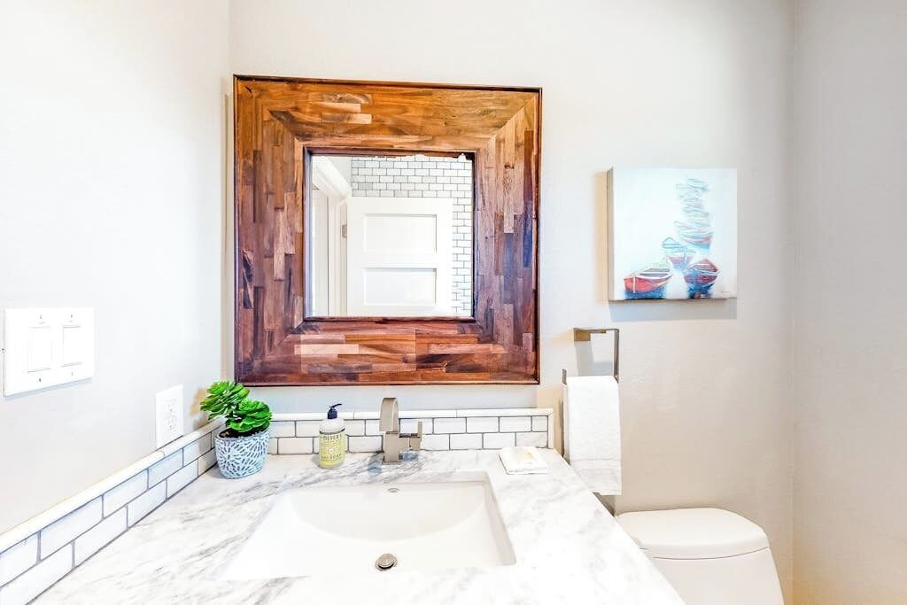 Une salle de bain avec un miroir à cadre en bois, un lavabo blanc, une plante en pot et des toilettes.