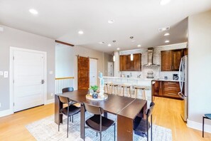 A modern kitchen with wooden cabinets, a stainless steel refrigerator, and a dining area with a dark wooden table and chairs. - Bright & Spacious Family Home With Firepit, Lake Views, Furnished Deck, Free Wifi (Leander)