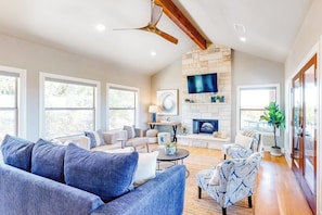 A spacious living room with a stone fireplace, large windows, and a ceiling fan. - Bright & Spacious Family Home With Firepit, Lake Views, Furnished Deck, Free Wifi (Leander)