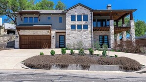 A two-story house with a stone facade, a large garage, and a covered porch area. - Bright & Spacious Family Home With Firepit, Lake Views, Furnished Deck, Free Wifi (Leander)