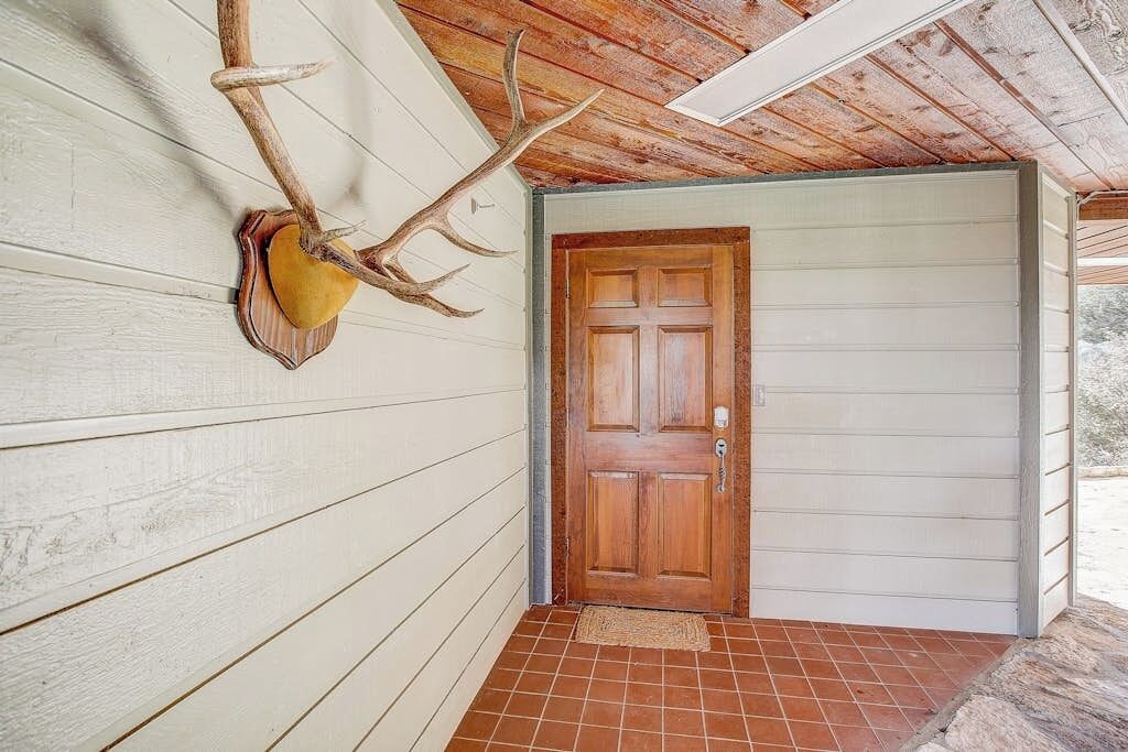 A wooden door with a glass panel, a mounted antler on the wall, and a tiled floor.