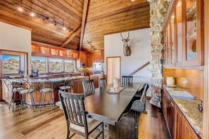 Una cocina amplia con una pared de acento de piedra, techo de madera y una mesa de comedor grande con sillas.