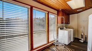 Een kamer met grote ramen, een wasmachine, een trolley en een plafondlamp.