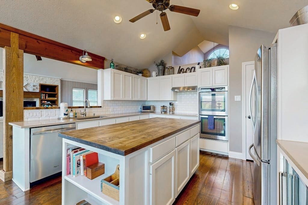 A kitchen with white cabinets, a wooden island, stainless steel appliances, and a ceiling fan.