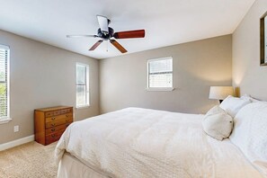 A bedroom with a bed, a ceiling fan, a dresser, and two windows with blinds. - Spacious Lakefront Hideaway With Decks, Grill, Billiards, Tennis & Pool (Spicewood)