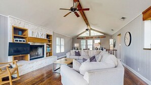 Ein geräumiges Wohnzimmer mit Kamin, einer großen Couch, einem Holztisch und einem Deckenventilator.