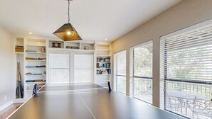 Ein Tischtennis-Tisch in einem Raum mit einem Bücherregal, einer Uhr und einem Schild mit der Aufschrift 'LIVING ROOM'.