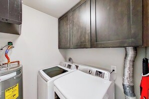 A laundry area with two white washing machines, a metal cabinet above, and a red tool hanging on the wall. - Contemporary, Dog-friendly Townhouse With Balcony, Pool & Day Docks (Horseshoe Bay)
