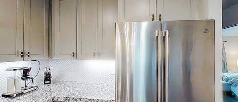 A modern kitchen with stainless steel appliances, a herringbone-patterned backsplash, and light-colored cabinetry.