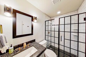 A bathroom with a large mirror, a sink, a toilet, and a shower enclosure with a tiled wall. - Contemporary, Dog-friendly Townhouse With Balcony, Pool & Day Docks (Horseshoe Bay)