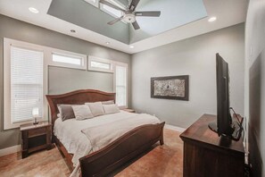 Ein Schlafzimmer mit einem Bett, einem Deckenventilator, einem Fernseher und einem gerahmten Kunstwerk an der Wand.