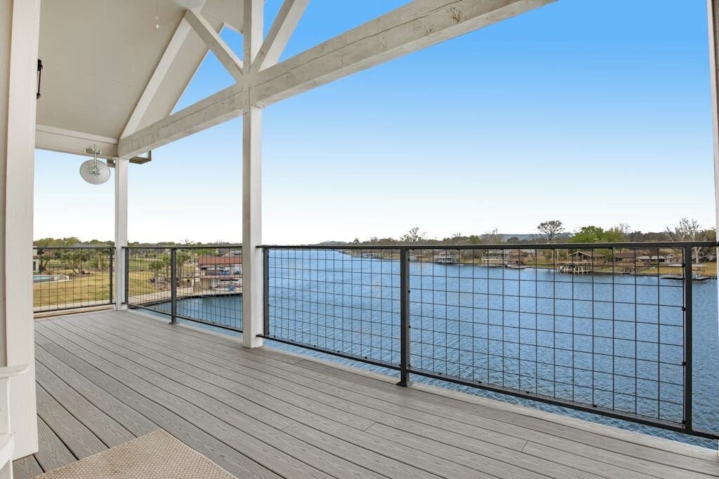 A covered deck with a view of a lake and distant buildings.