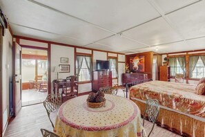 A room with a bed, a television, a dining table with chairs, a fireplace, and a window. - Historic Lakefront & Wildlife Haven With Firepit & Gas Grill - Minutes to Water (Burnet)