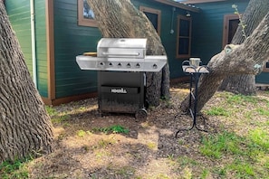 A backyard with a grill, trees, and a house with green siding. - Historic Lakefront & Wildlife Haven With Firepit & Gas Grill - Minutes to Water (Burnet)