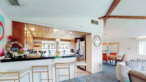 Eine moderne Küche mit Bar, Holzbalkendecke und Essbereich mit einer Couch und Stühlen.