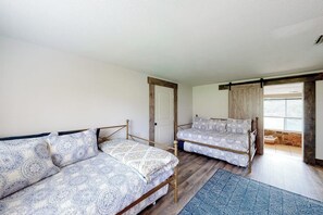 Een kamer met twee bedden, een houten vloer, een groot raam en een deur.