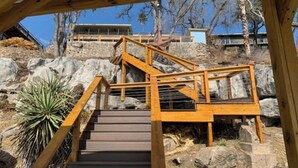 Eine Holztreppe führt einen steilen, felsigen Hang hinauf, mit Blick auf ein Gebäude im Hintergrund.