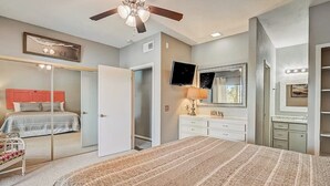 Un dormitorio con cama, ventilador de techo, televisor, espejo y cómoda.