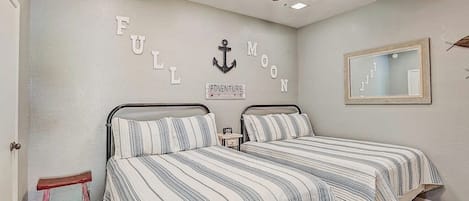 Un dormitorio con dos camas, un ventilador de techo, un taburete pequeño y un espejo fijado a la pared.