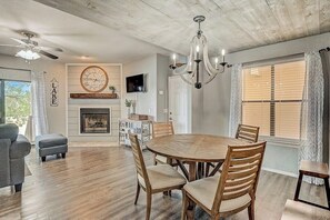 A dining area with a round wooden table, four wooden chairs, a chandelier, a fireplace, and a clock on the wall. - Dog-friendly Water View Condo With Inviting Porch, AC, W/d, & Modern Charm (Horseshoe Bay)
